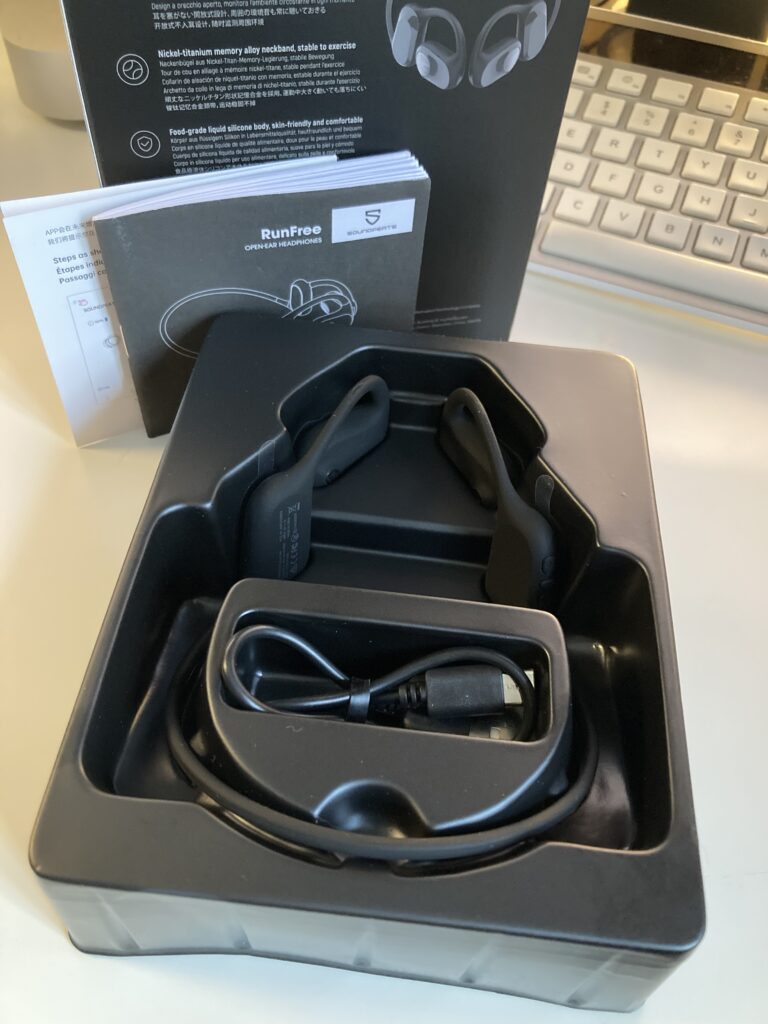 The inside of the box showing the RunFree Open-ear Headphones, charging cable and information booklets